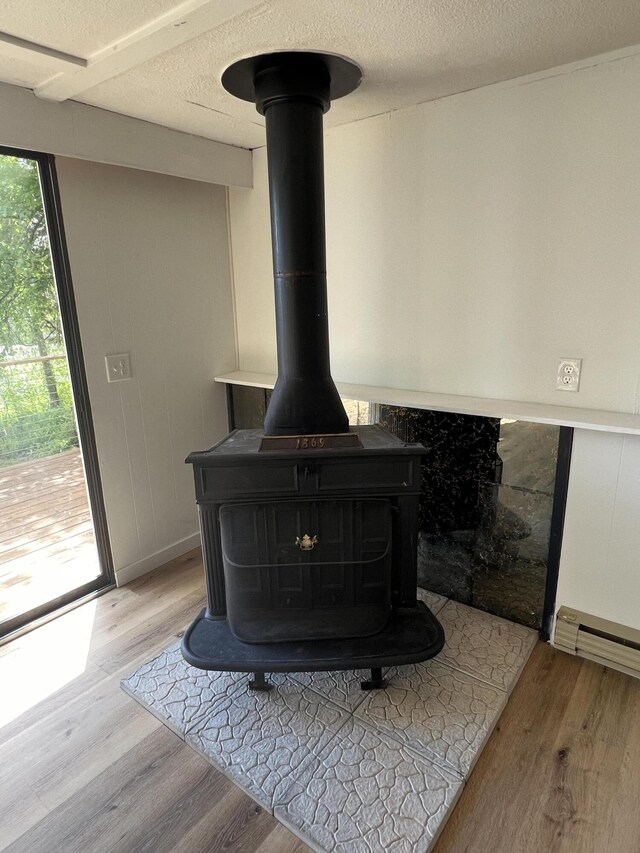 interior details with a wood stove, wood finished floors, baseboard heating, and a textured ceiling