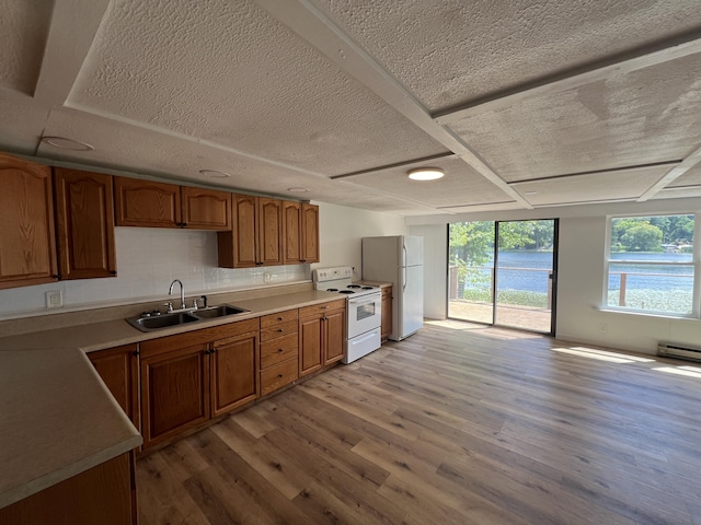 kitchen featuring brown cabinets, light wood finished floors, a sink, white appliances, and light countertops