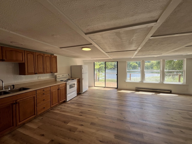 kitchen featuring brown cabinets, a sink, wood finished floors, white appliances, and baseboard heating