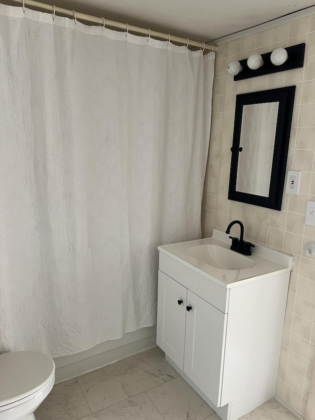 bathroom with marble finish floor, vanity, tile walls, and toilet