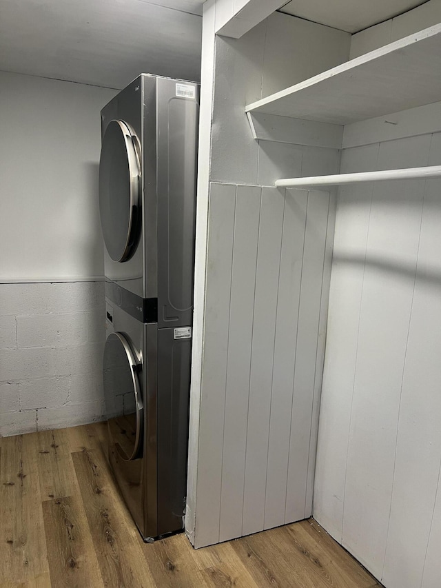 laundry room with laundry area, wood finished floors, concrete block wall, and stacked washer and dryer