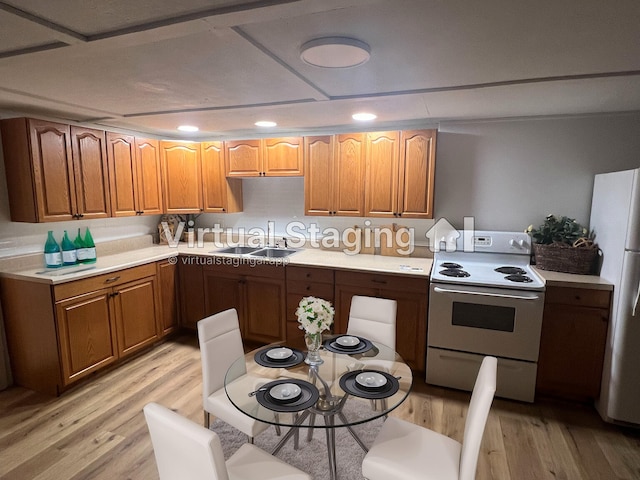 kitchen featuring a sink, white appliances, brown cabinetry, light wood finished floors, and light countertops