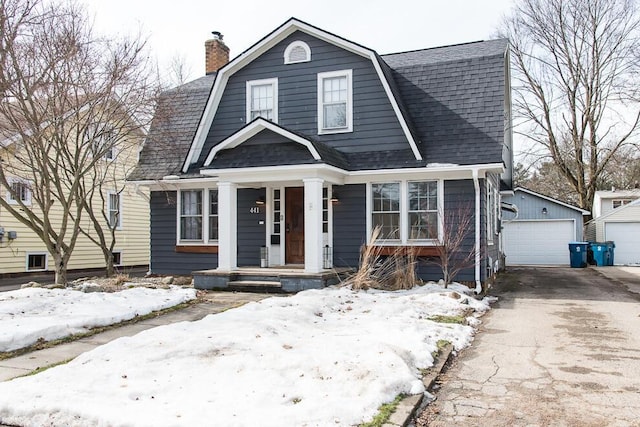 colonial inspired home with a gambrel roof, a porch, roof with shingles, a garage, and an outdoor structure