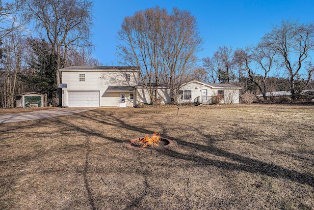 view of front facade with concrete driveway, a fire pit, a garage, and a front lawn