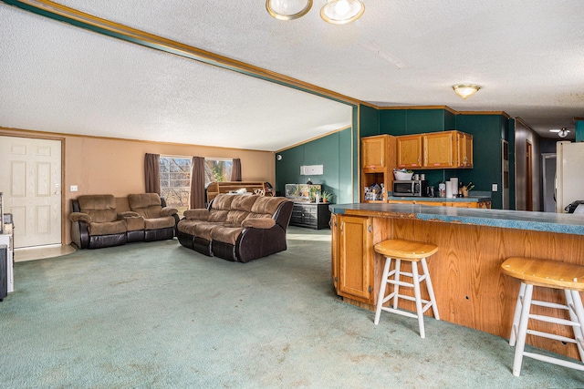 kitchen with stainless steel microwave, a kitchen breakfast bar, light colored carpet, and vaulted ceiling