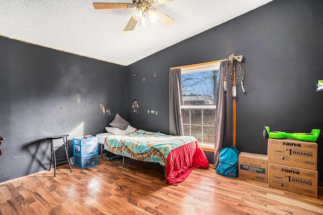 bedroom featuring ceiling fan, a textured ceiling, wood finished floors, and vaulted ceiling