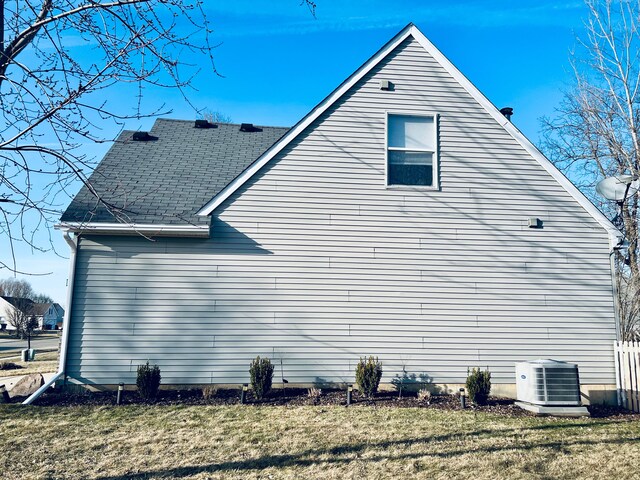 view of home's exterior with cooling unit, a lawn, and a shingled roof