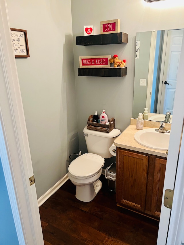 half bathroom with vanity, toilet, wood finished floors, and baseboards