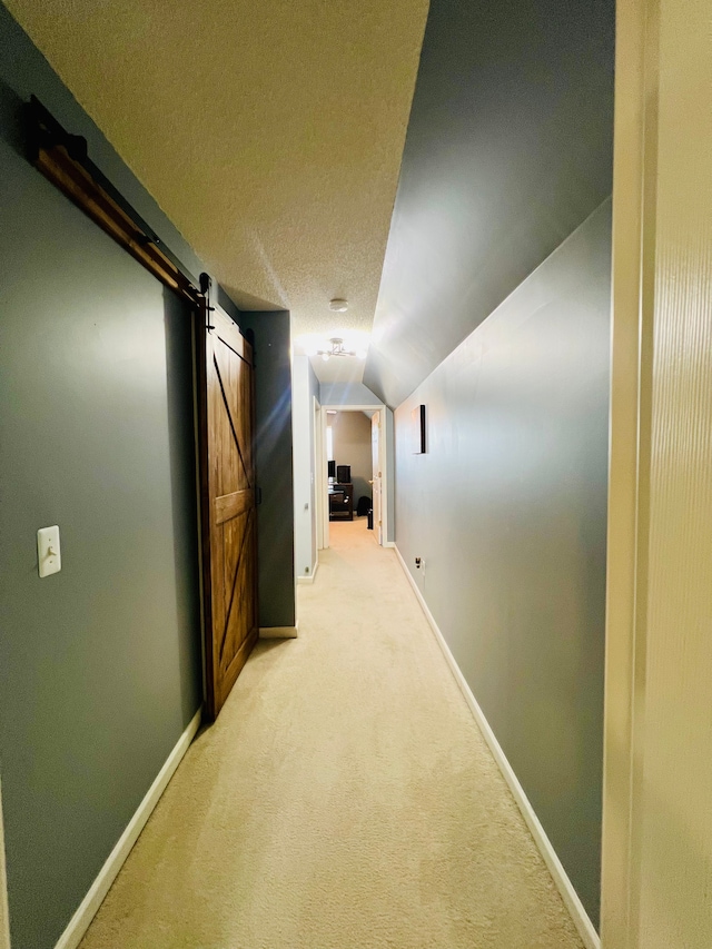 hall with baseboards, vaulted ceiling, a textured ceiling, a barn door, and light carpet