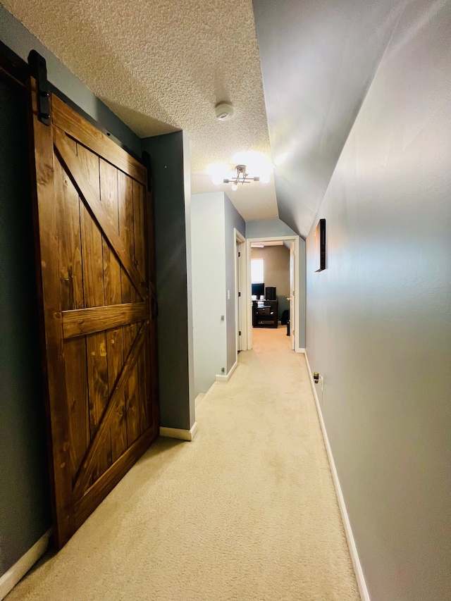 hall with light carpet, a textured ceiling, a barn door, baseboards, and vaulted ceiling