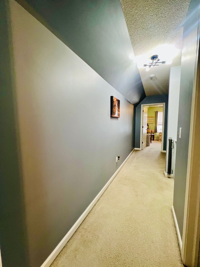 hall featuring baseboards, light carpet, a textured ceiling, and lofted ceiling