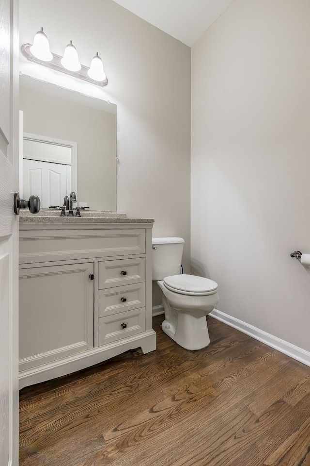 half bathroom with vanity, toilet, wood finished floors, and baseboards