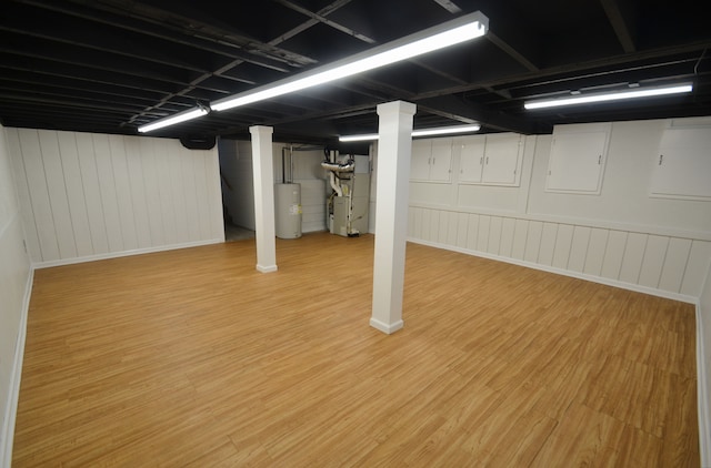 finished basement featuring heating unit, water heater, and wood finished floors