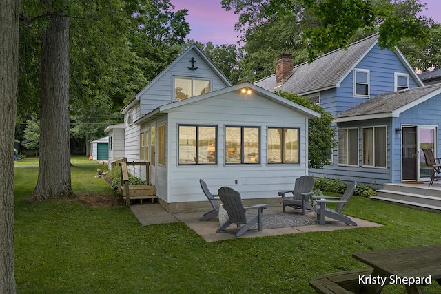 back of property at dusk with a yard, a patio, a chimney, and a shingled roof