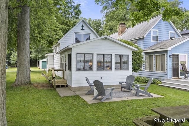 rear view of property with a yard, a patio area, roof with shingles, and a chimney