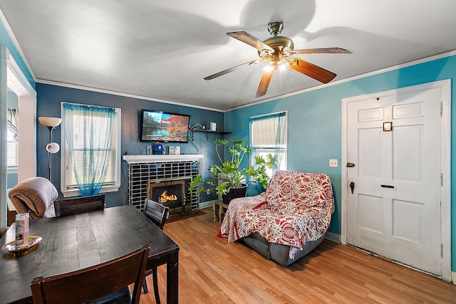 living room with a tiled fireplace, a ceiling fan, light wood-type flooring, and ornamental molding