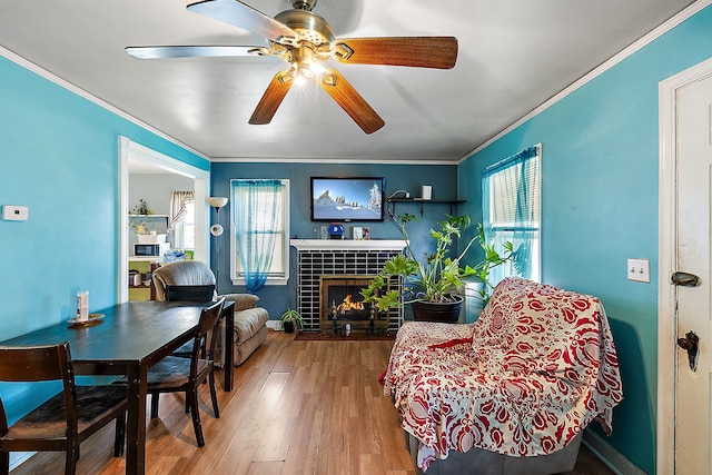 living area with a fireplace, crown molding, a ceiling fan, and wood finished floors