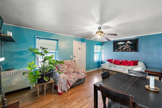 living room featuring a ceiling fan, wood finished floors, baseboards, radiator heating unit, and ornamental molding