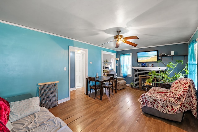 living area featuring baseboards, wood finished floors, ornamental molding, and a tile fireplace