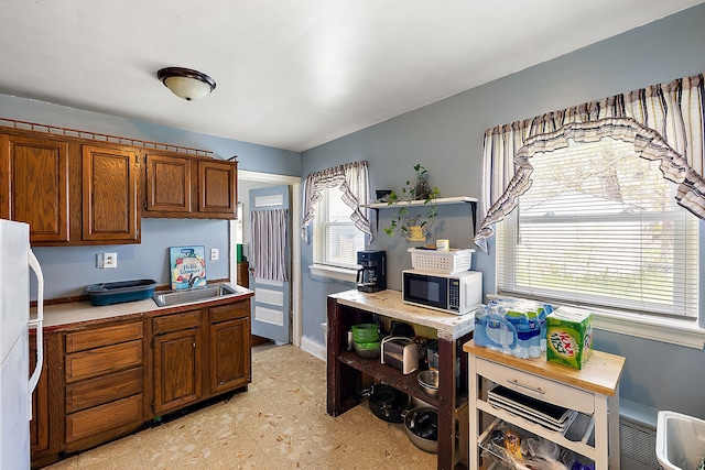 kitchen featuring brown cabinetry, baseboards, open shelves, freestanding refrigerator, and a sink