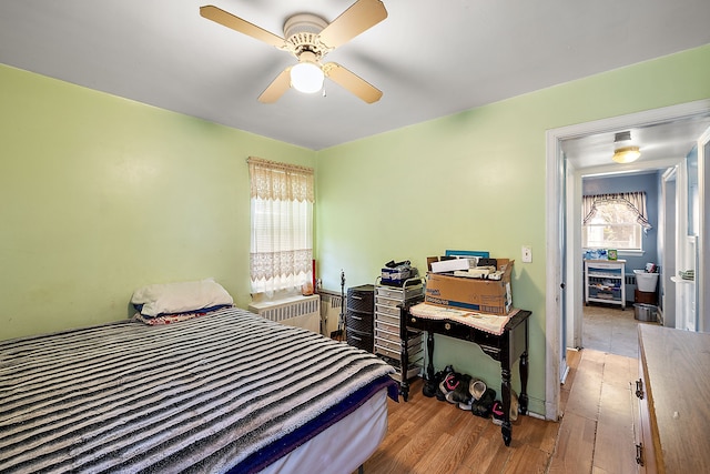 bedroom with radiator, wood finished floors, and a ceiling fan