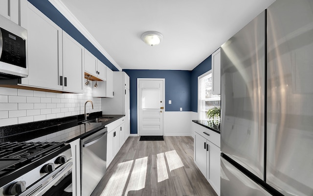 kitchen featuring a sink, tasteful backsplash, white cabinetry, light wood-style floors, and appliances with stainless steel finishes