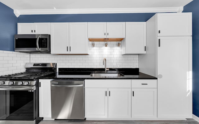 kitchen featuring a sink, stainless steel appliances, white cabinets, crown molding, and tasteful backsplash