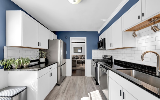 kitchen with dark stone counters, a sink, stainless steel appliances, white cabinetry, and light wood-type flooring