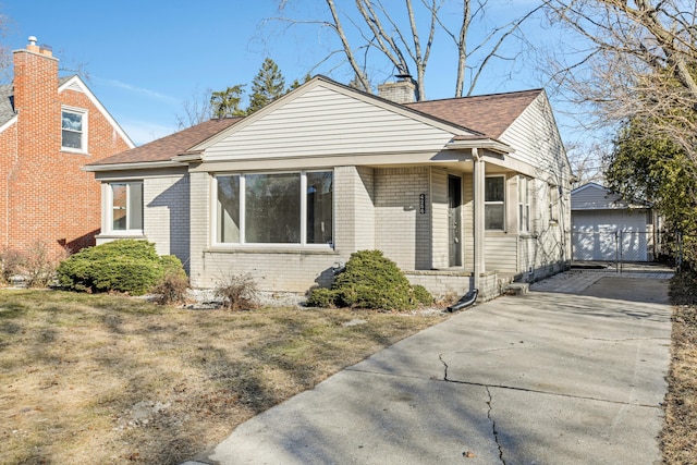 bungalow-style house featuring brick siding, a shingled roof, a chimney, a garage, and an outbuilding