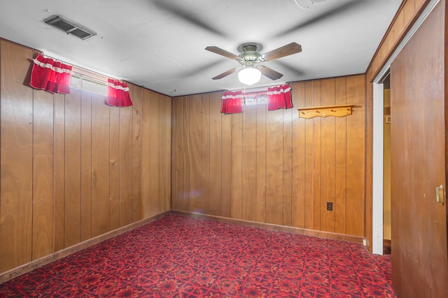 empty room featuring a ceiling fan, baseboards, visible vents, and wood walls