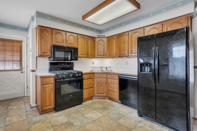 kitchen featuring wallpapered walls, light countertops, brown cabinetry, black appliances, and a sink