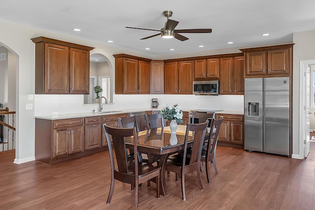 kitchen featuring wood finished floors, arched walkways, a sink, light countertops, and appliances with stainless steel finishes