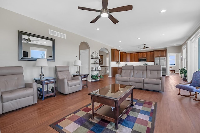 living room featuring arched walkways, visible vents, a wealth of natural light, and wood finished floors