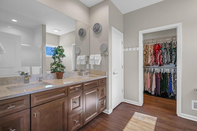 bathroom with double vanity, a spacious closet, wood finished floors, and a sink