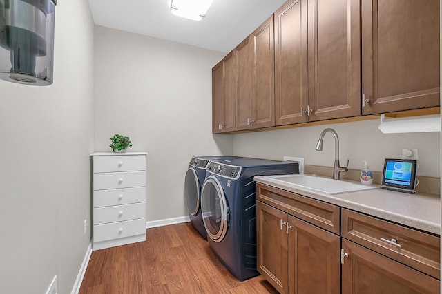 laundry area featuring a sink, cabinet space, light wood finished floors, baseboards, and washing machine and clothes dryer