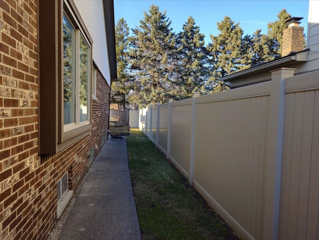 view of side of property featuring fence, brick siding, and a chimney