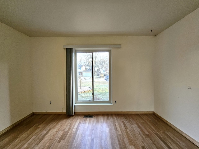 unfurnished room featuring wood finished floors, visible vents, and baseboards