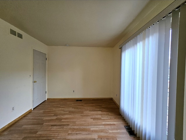 empty room with visible vents, light wood-type flooring, and baseboards