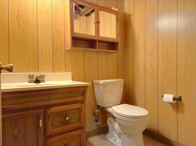 half bathroom featuring wooden walls, toilet, and vanity