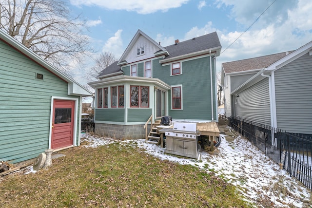 snow covered rear of property with fence and a sunroom