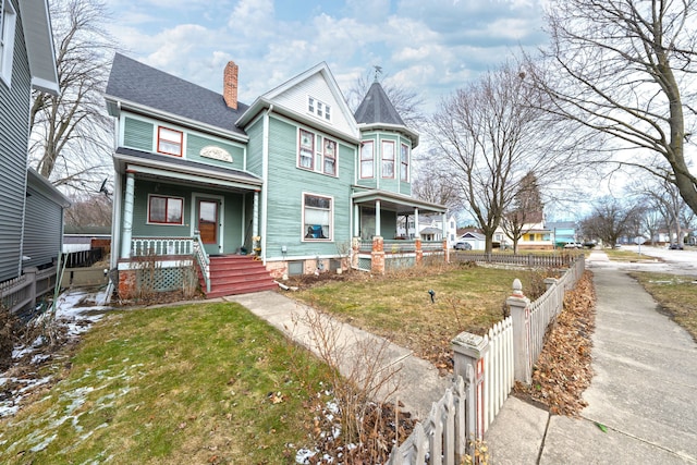 victorian house featuring a shingled roof, fence, a porch, a front yard, and a chimney