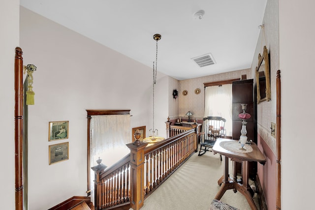 hallway featuring an upstairs landing, visible vents, and carpet floors