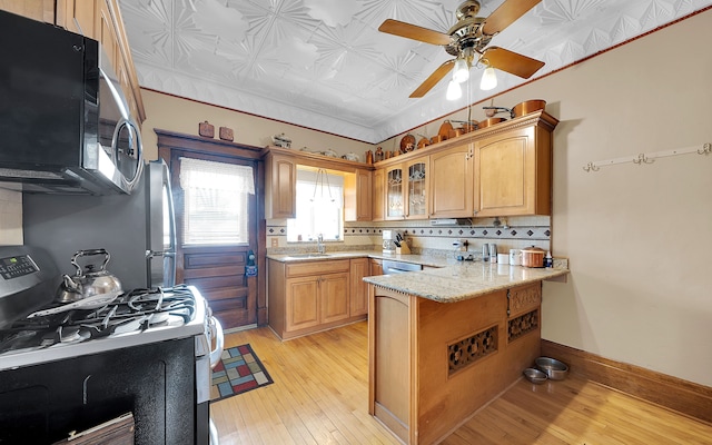 kitchen featuring stainless steel microwave, backsplash, baseboards, gas range oven, and a peninsula