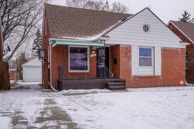 bungalow-style home featuring brick siding, a detached garage, an outbuilding, and roof with shingles