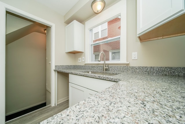 kitchen featuring light stone counters, wood finished floors, baseboards, a sink, and white cabinets