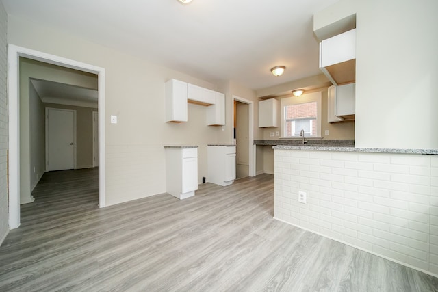 kitchen with light wood-type flooring, light stone counters, a peninsula, white cabinets, and a sink