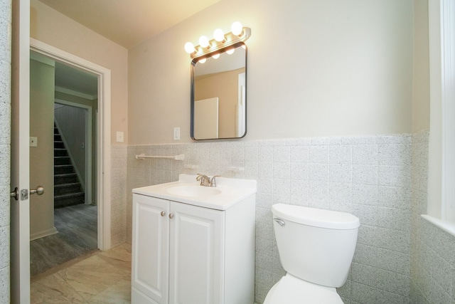 bathroom featuring a wainscoted wall, toilet, vanity, and tile walls