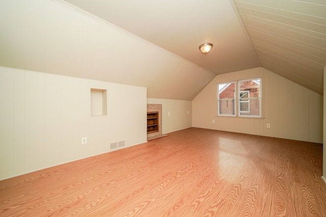 bonus room with visible vents, lofted ceiling, a fireplace with raised hearth, and wood finished floors