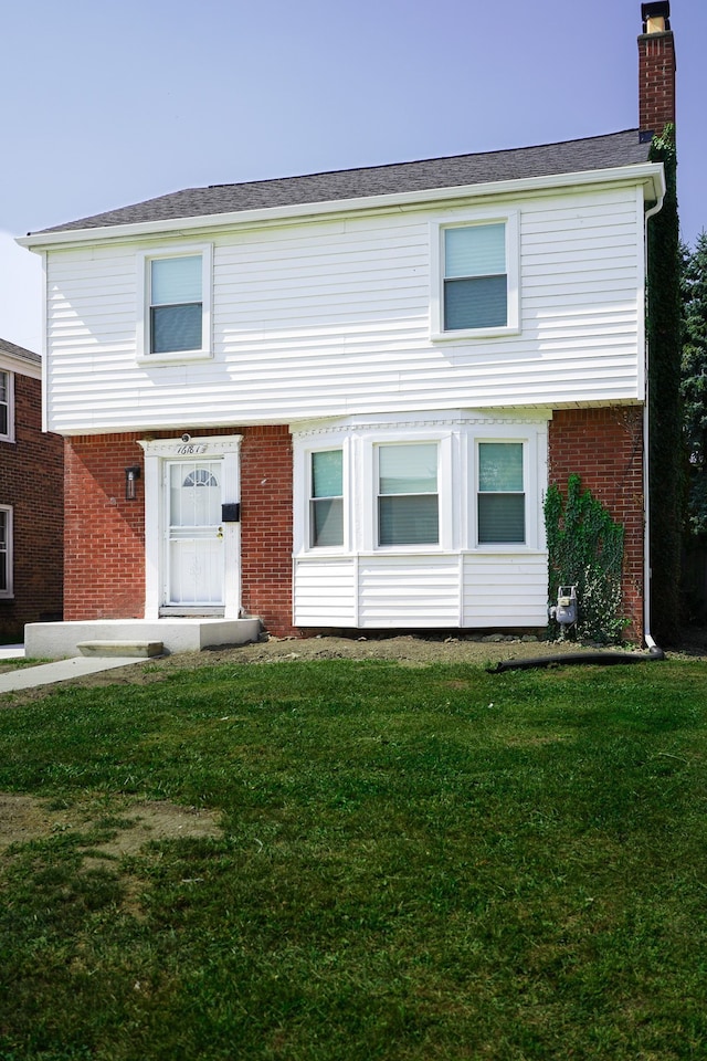 view of front of house with brick siding, a chimney, and a front lawn