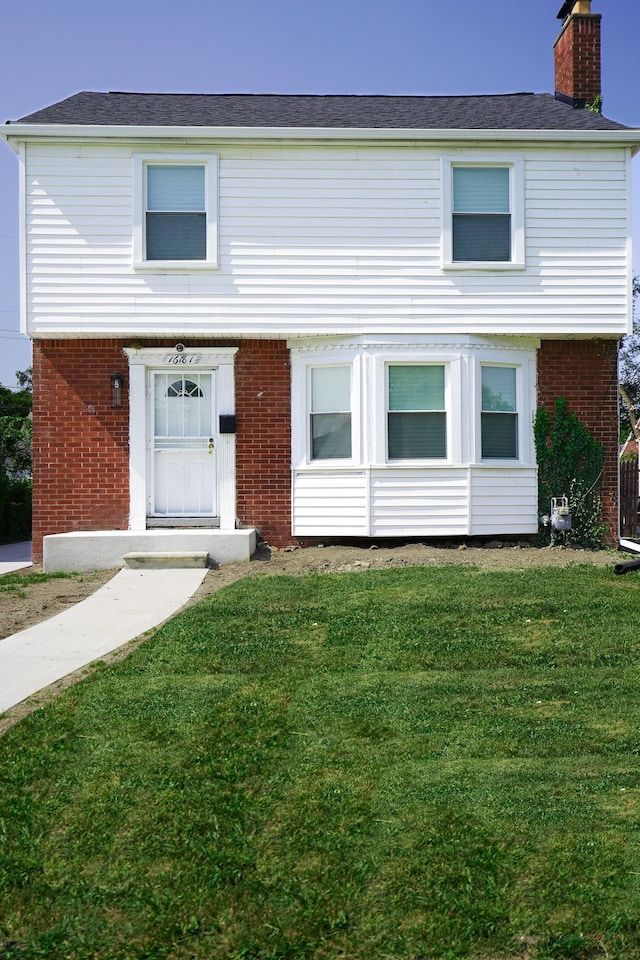 colonial house with brick siding, a chimney, and a front yard